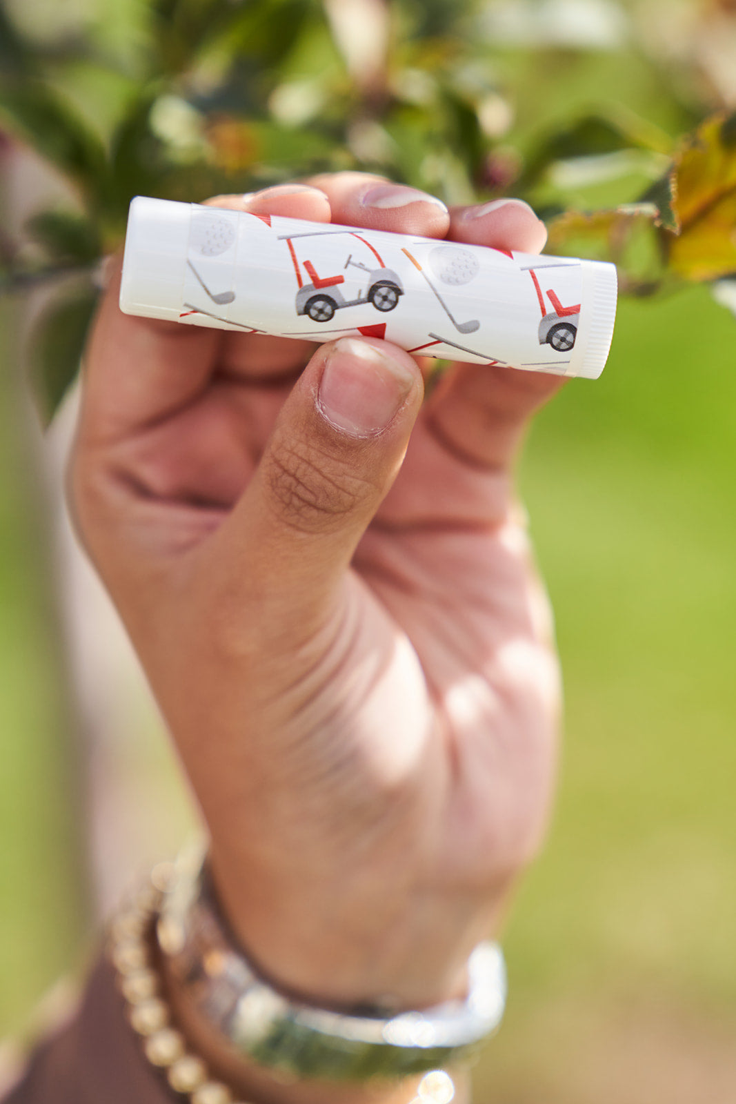 Gold cart, gold club and ball red, black and white golf doodles. Being held in a womans hamd with a blurred tree in the background.