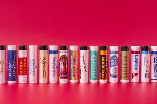 Lip balm with various business labels all standing up on a red background