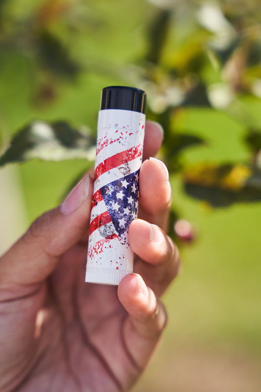 Distressed, speckeld flag on a white lip balm tube. Being held in a womans hand. 
