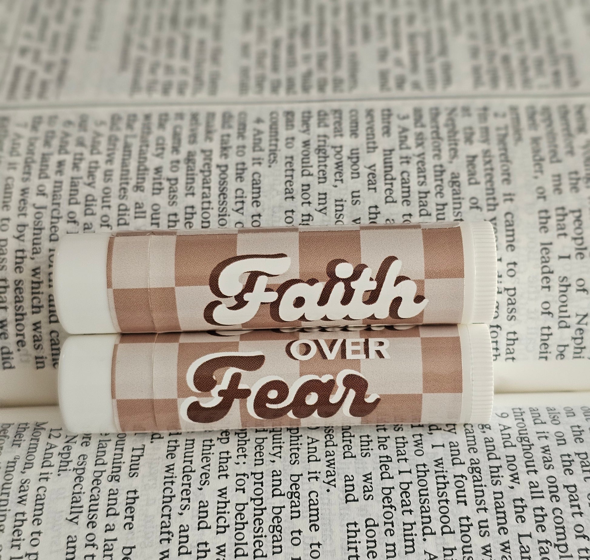 Brown and tan checkered background that says faith over fear in a groovy font. Laid on open scriptures. 
