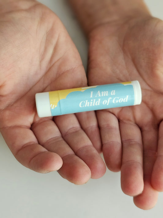 Blue design with bright yellow son lip balm that says i am a child of god. Being held in the open hands of a child. 