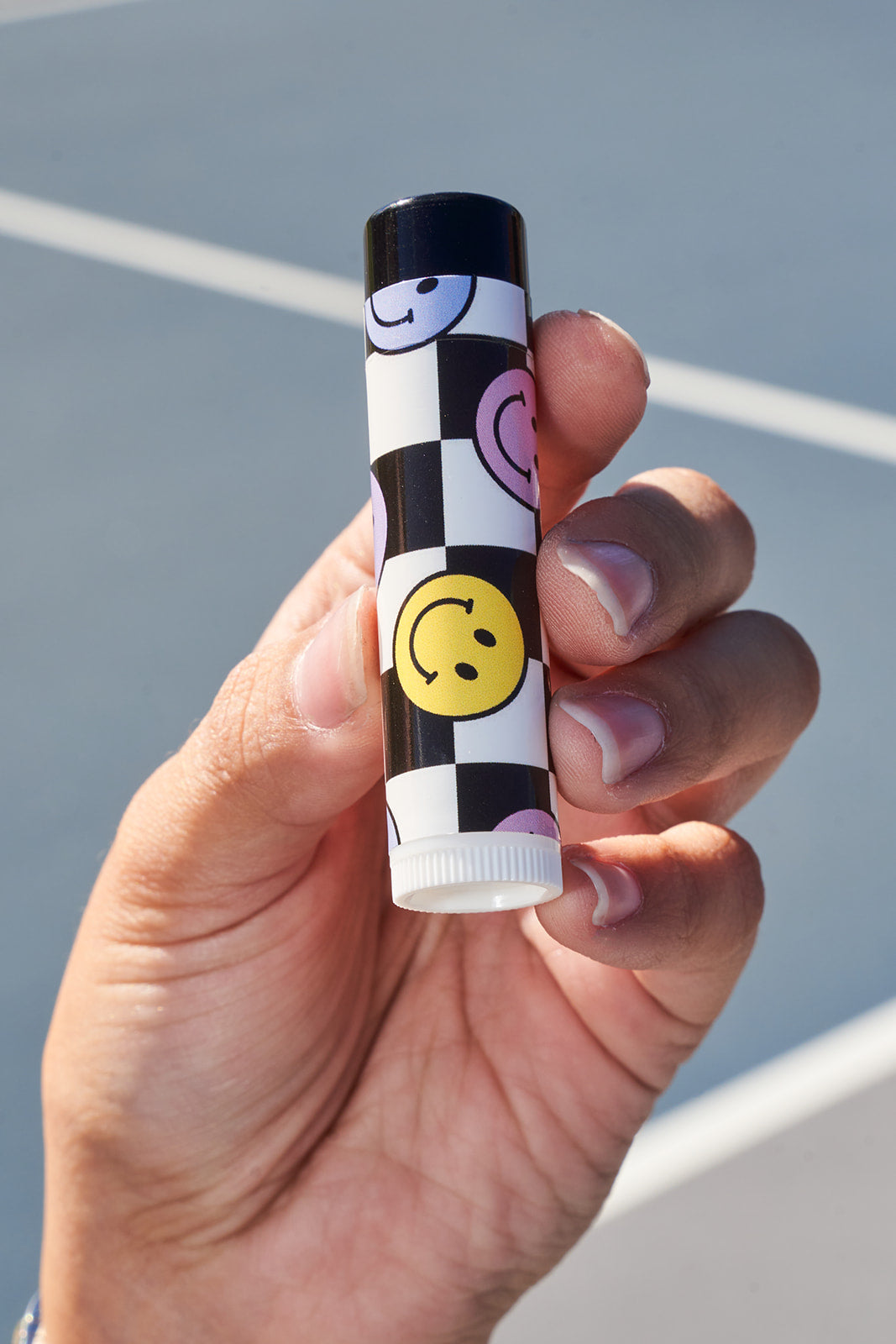 Hand holding a lip balm with smiley face design against a gray background