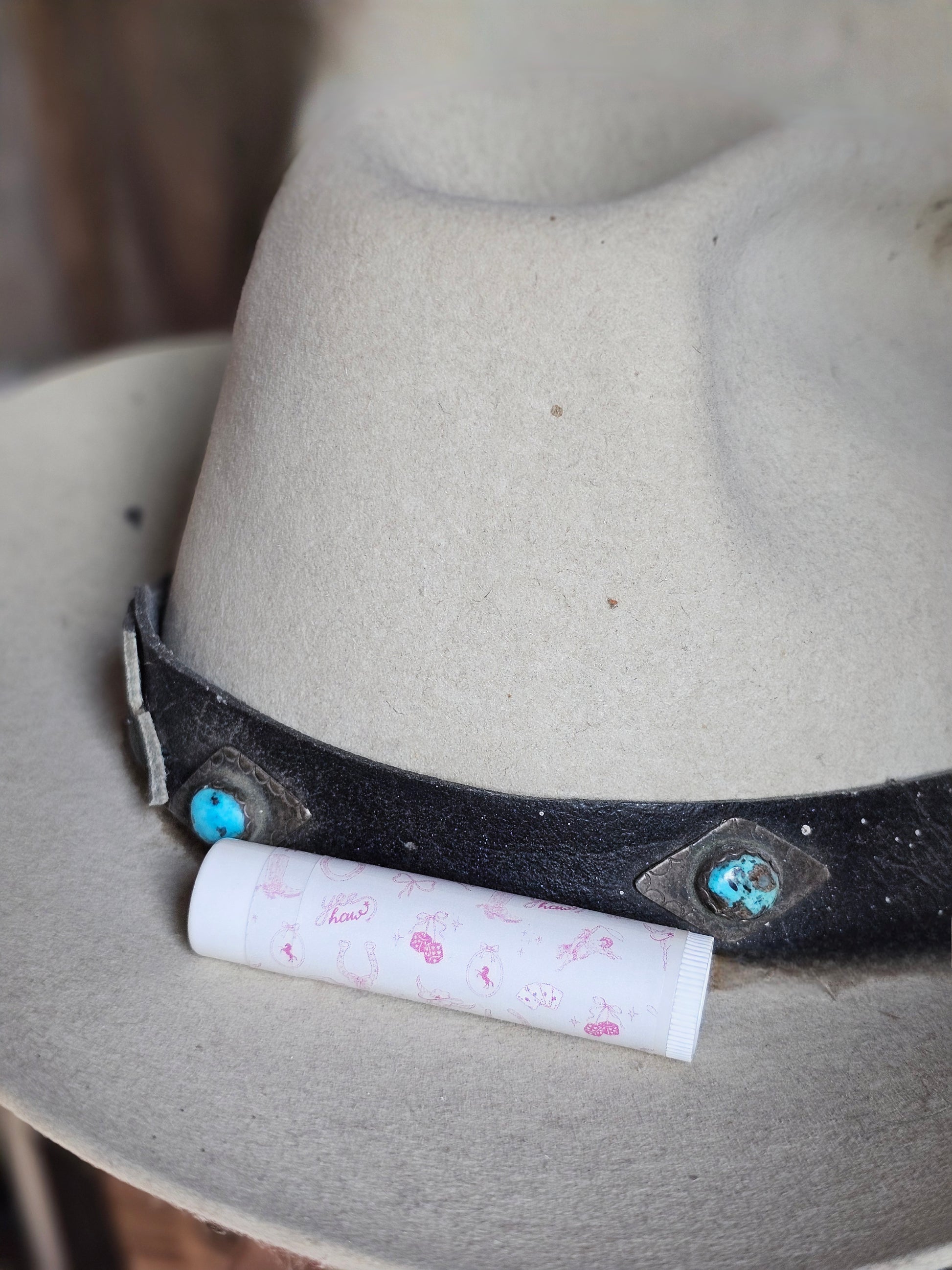 Western Kiss lip balm. White background, pink western doodles, boots, rope, bows dice, cowgirl hat. 